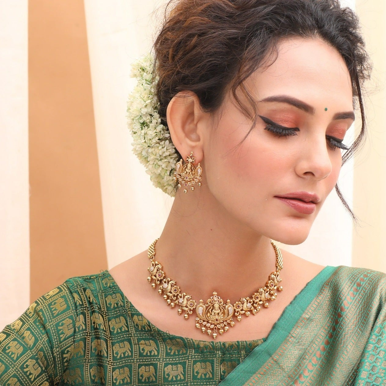 A picture of an Indian artificial jewelry set: an antique gold-toned necklace and earrings with Goddess Laxmi motifs on a white background