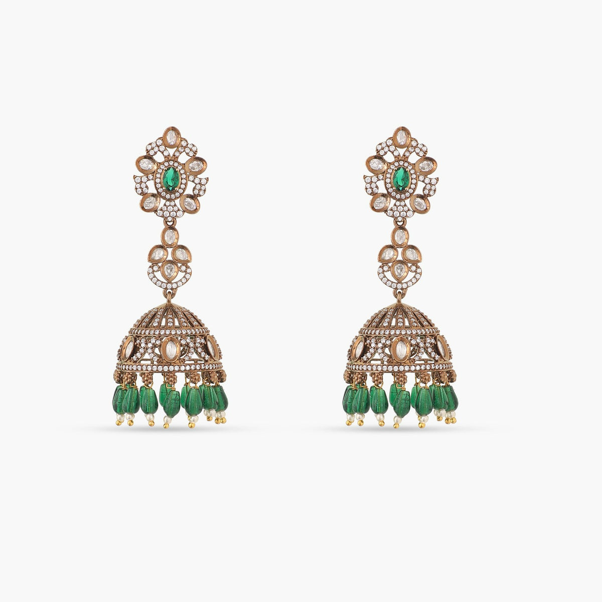 A picture of a pair of Indian artificial jhumka earrings with green gemstones and Cubic Zirconia stones on a white surface.