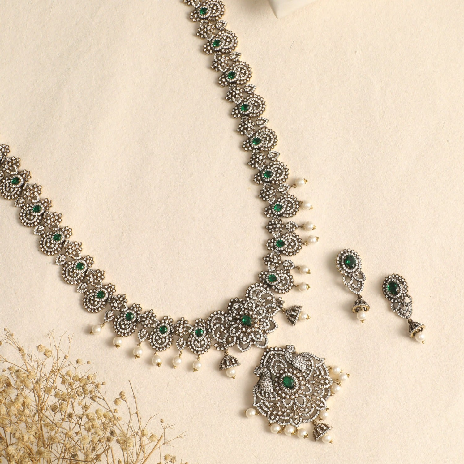 A picture of an Indian artificial jewelry set: an antique plated necklace and earrings set with green gemstones and Cubic Zirconia on a white background.