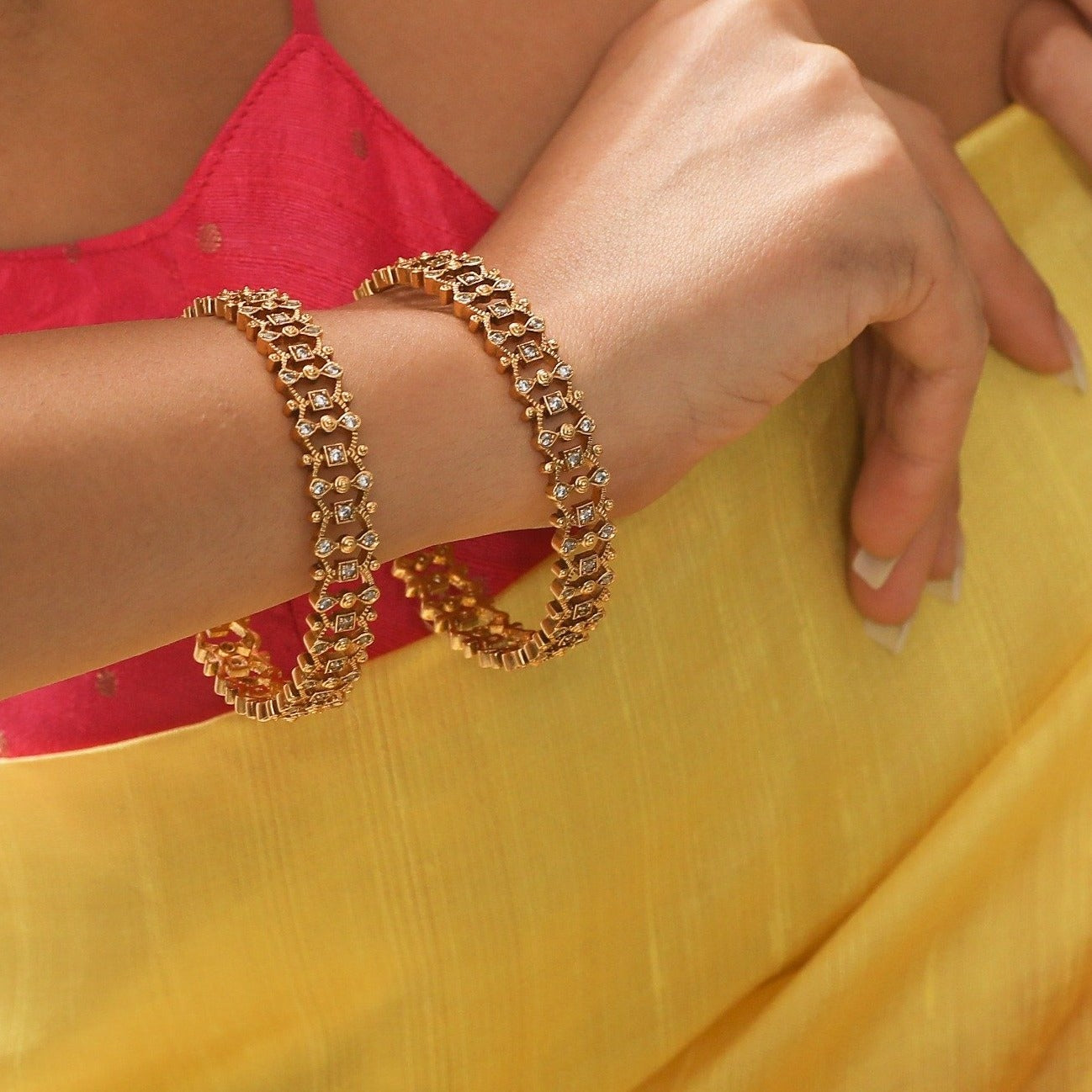 A picture of Indian artificial jewelry: a pair of gold-colored bangles with red and Cubic zirconia stones on a white background.