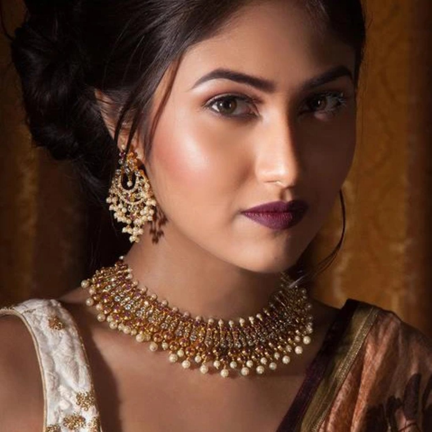 A picture of Indian artificial jewelry. It is a gold plated necklace set with earrings featuring pearls and green and red gemstones.