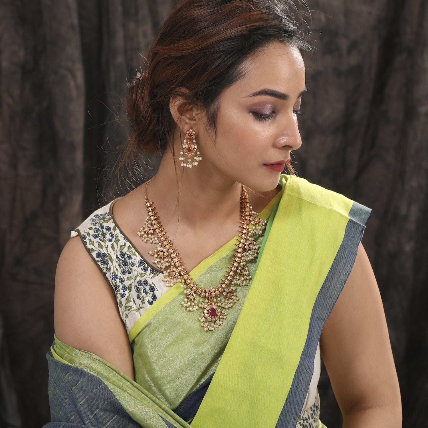 A picture of an Indian artificial jewelry set featuring a gold plated necklace and earrings embellished with pearls and green gemstones.