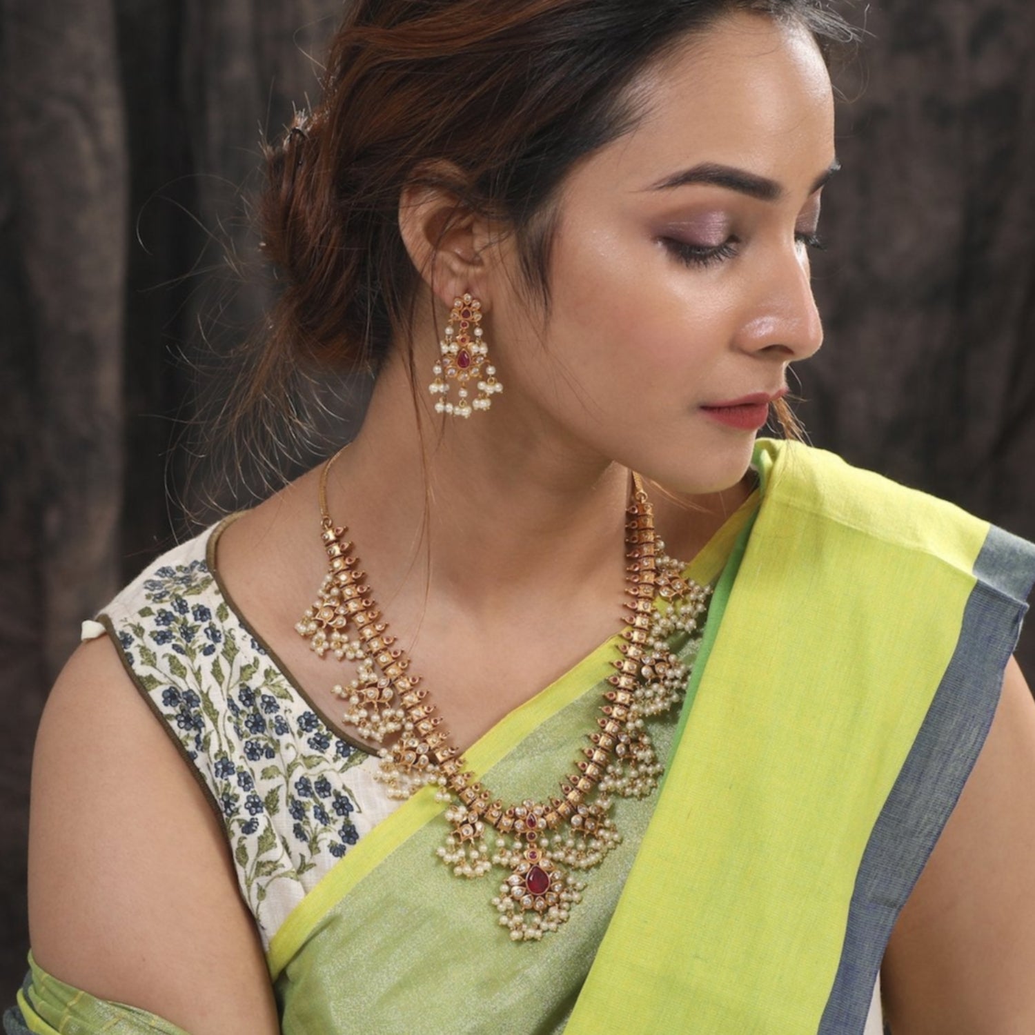 A picture of an Indian artificial jewelry set featuring a gold plated necklace and earrings embellished with pearls and green gemstones.