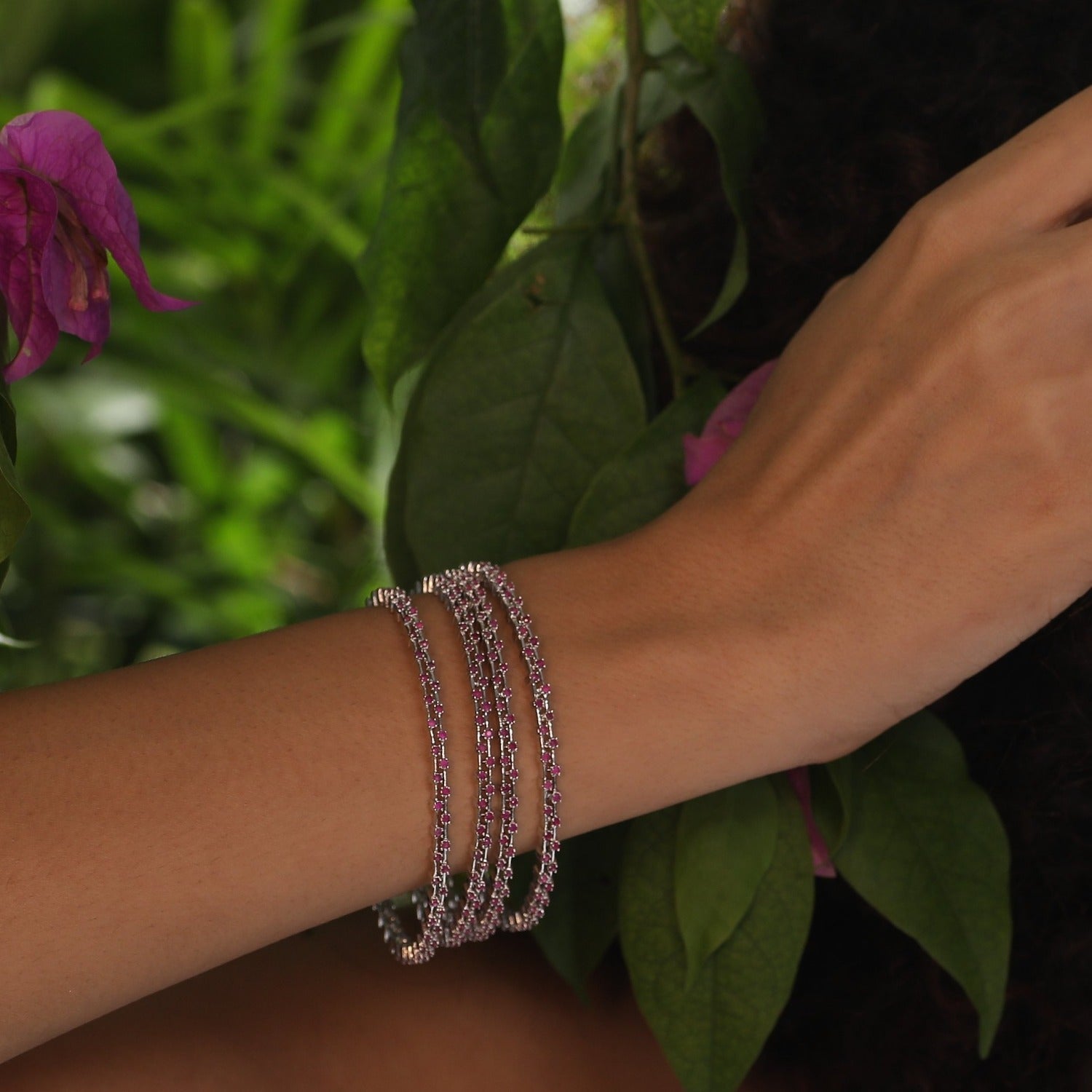 A close-up image of a pair of gold plated bangles with green gemstones on a white background.