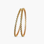 A close-up image of a pair of gold plated bangles with green gemstones on a white background.