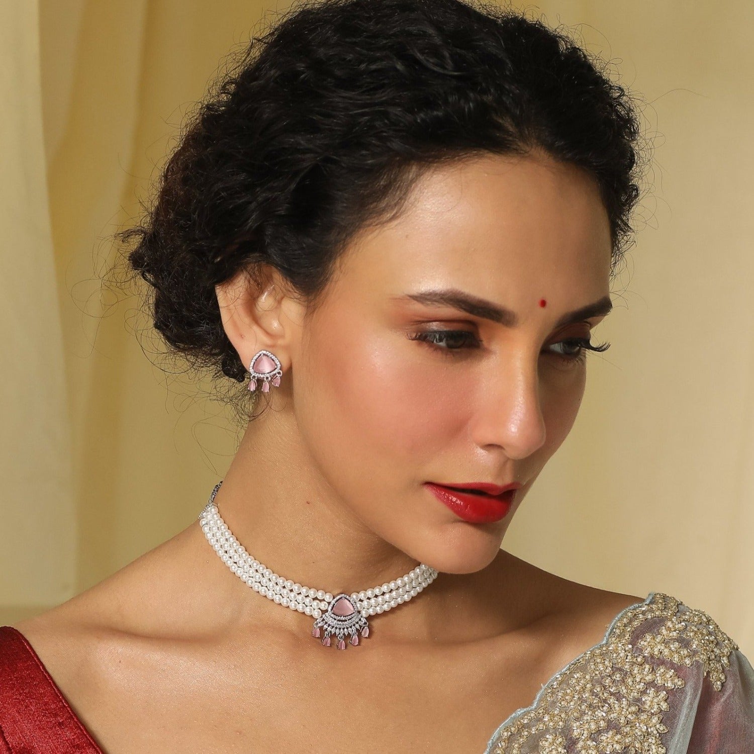 A picture of an Indian artificial jewelry set: a three layered pearl necklace and earrings featuring Cubic Zirconia and green gemstones.