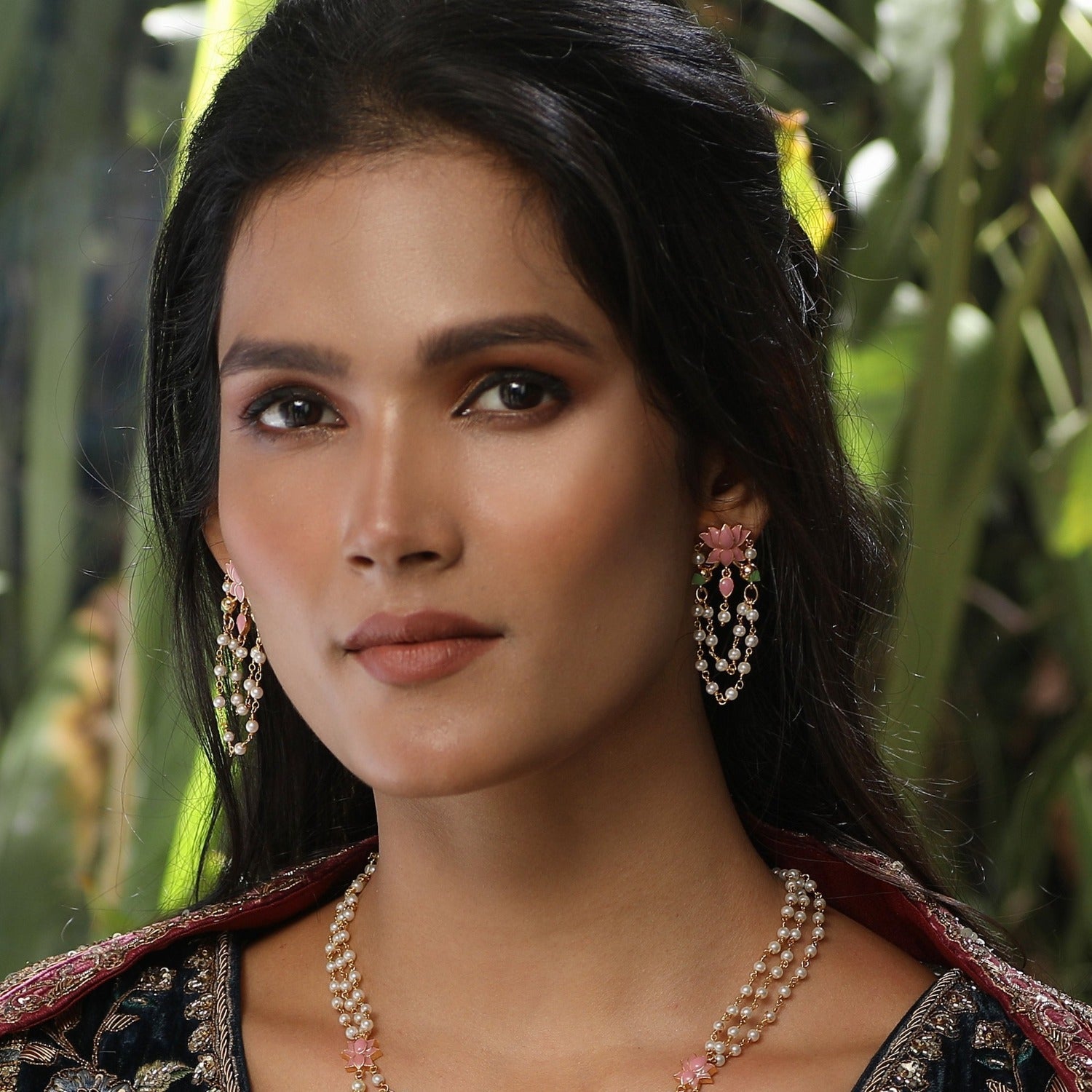 A picture of Indian artificial earrings: a pair of chandelier earrings with pink and green gemstones with white beads on a white background.